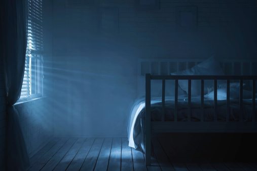 Bed in a dark room with light streaming in