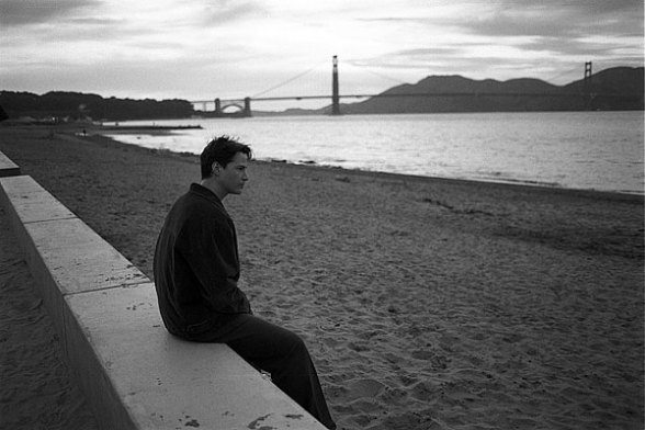 black and white photo of man sitting on ledge in sand