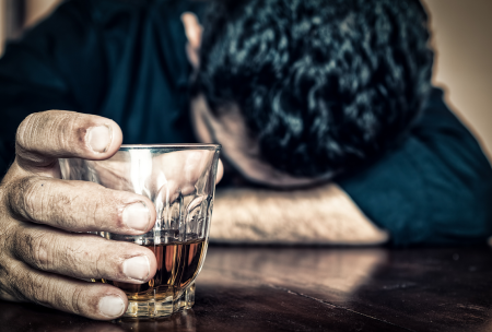Man with head on table holding glass of alcohol