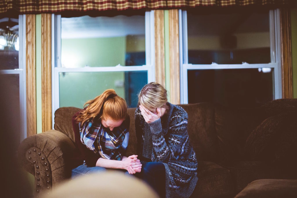 Two women crying together on couch
