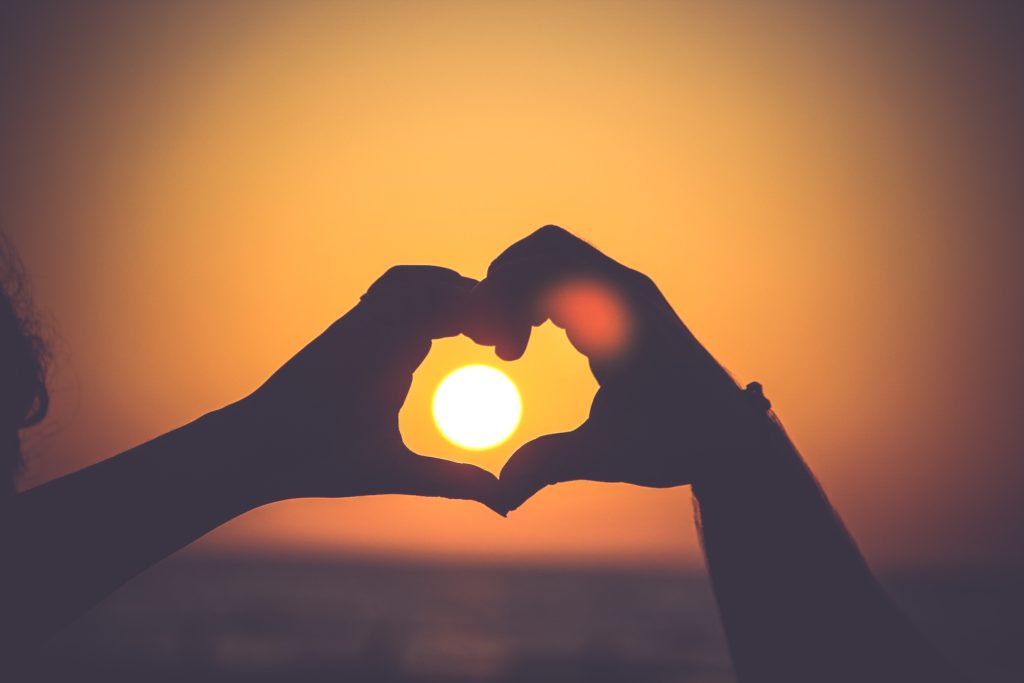 Hands in the shape of a heart over sun