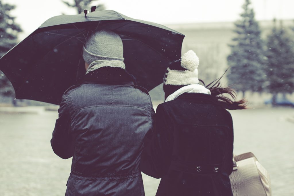 Two people walking in rain with umbrella