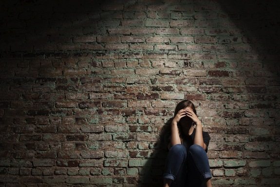 Woman crouched against brick wall