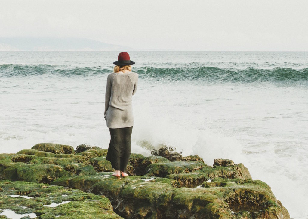 Woman standing at cliff's edge looking out at the waves
