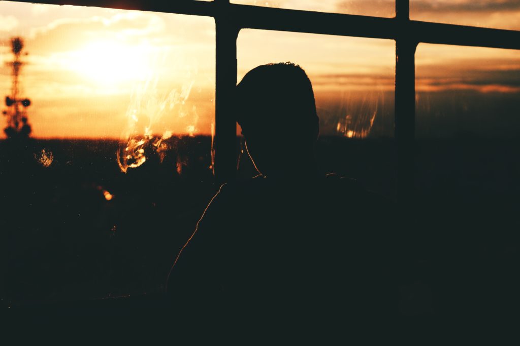 Silhouette of man looking out a window during sunset