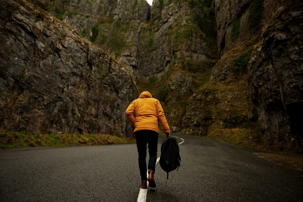 Person walking with backpack up road between rocky mountains