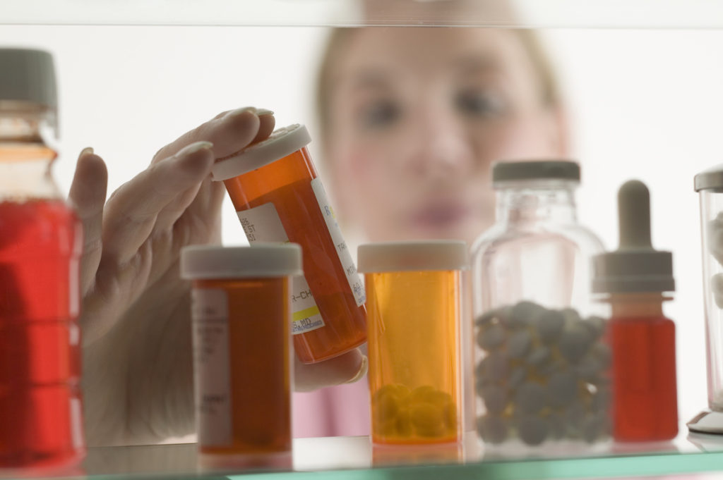 Woman opening up medicine cabinet of prescription bottles