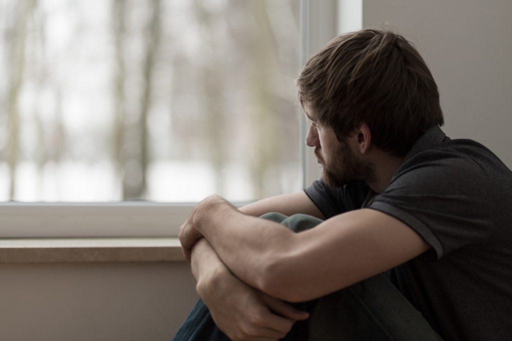Man crouched looking out at window