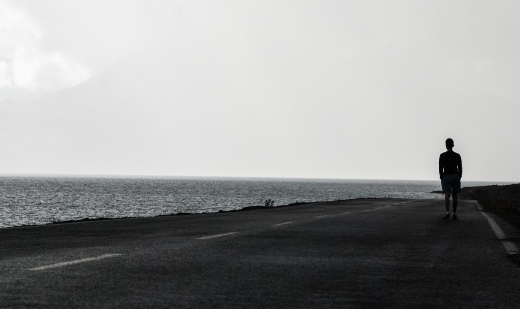 Man walking down road along water