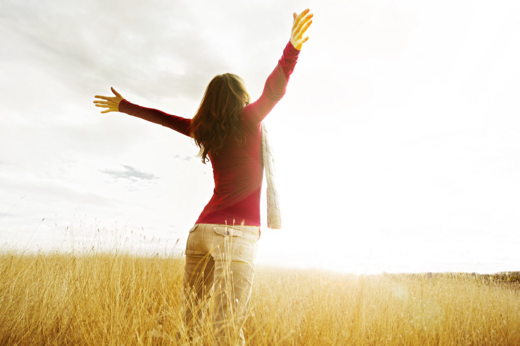 Woman standing in field facing sun with arms stretched out
