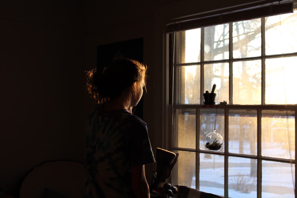Teenage girl staring out window in dark room