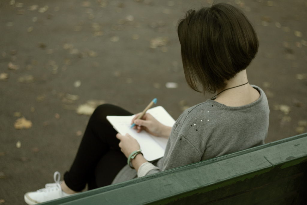 Woman sitting on bench writing into notebook