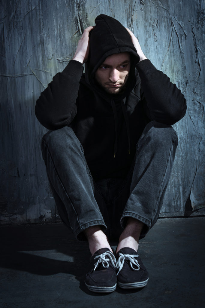 Man crouched sitting against wall in dark clothes