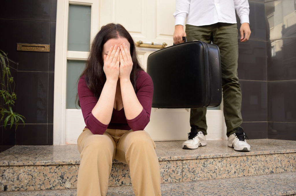Woman sitting on stoop with head in hands with man and luggage behind her