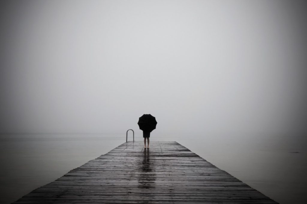 Person standing at the end of a pier holding an umbrella on a stormy day