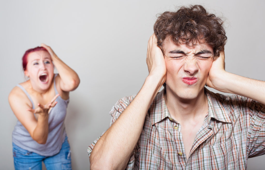 Man covering his ears while woman is yelling behind him