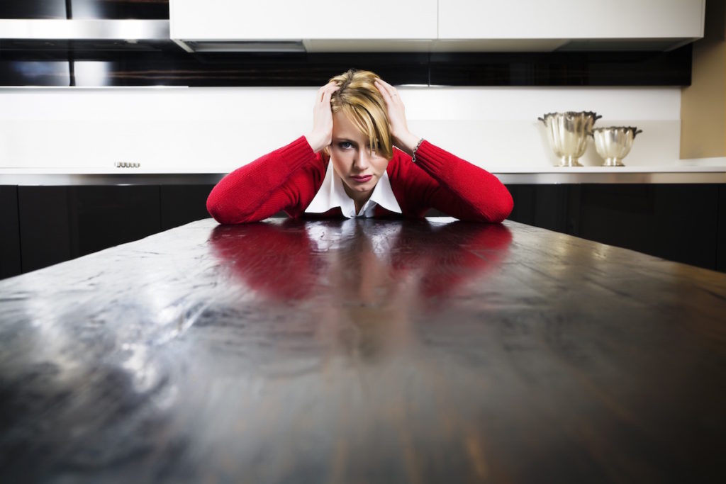 Woman sitting at the end of a long table with head in hands