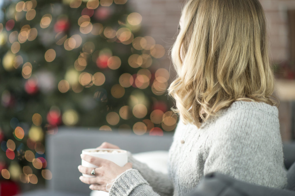 Woman sitting on couch with hot chocolate and Christmas tree in the background