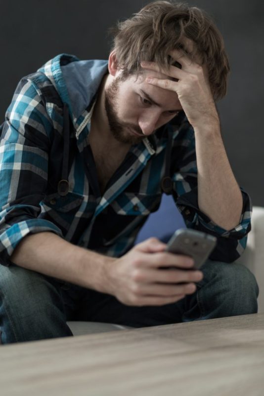 Man leaning over holding phone and holding head