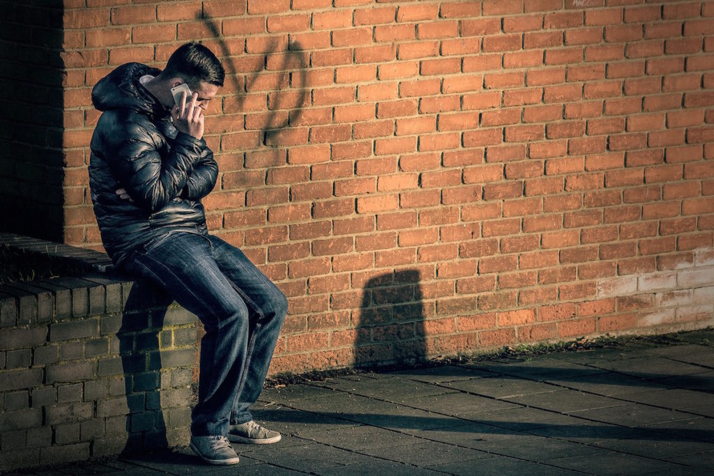 Man sitting on brick ledge talking on mobile phone