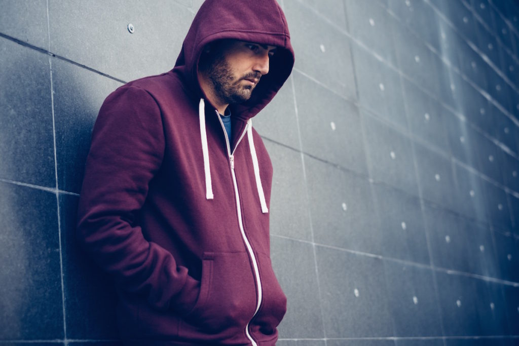 Man with hoodie leaning against a wall looking down