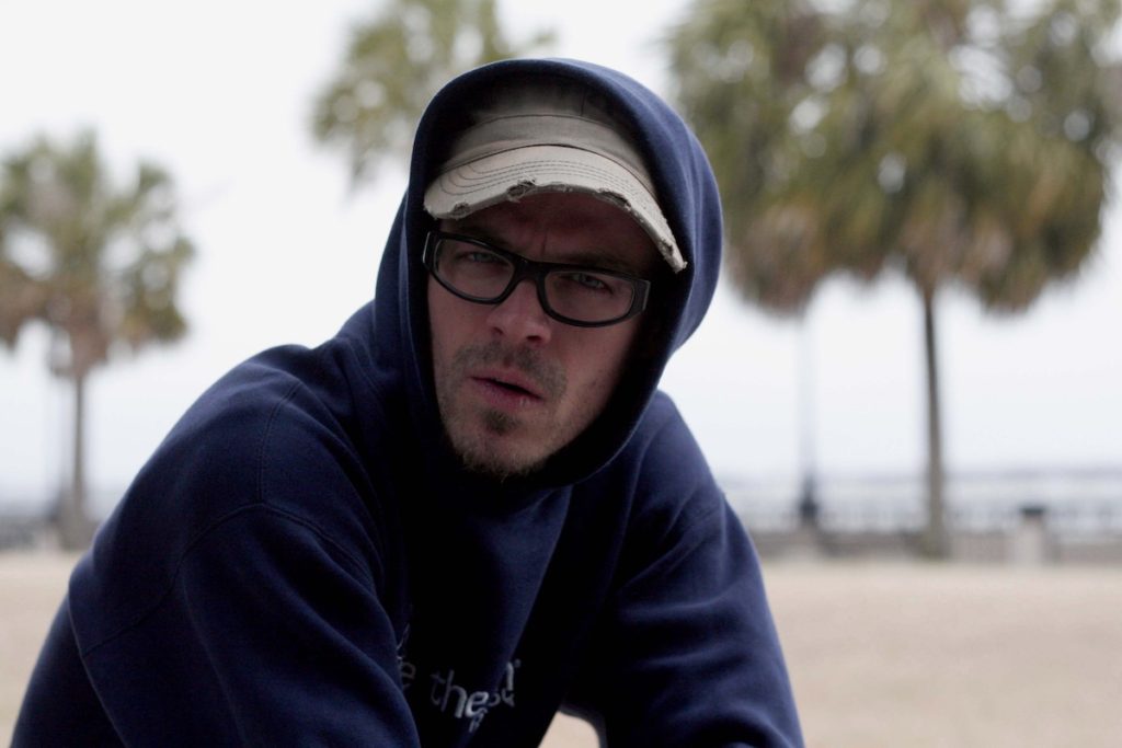 Young man in hat, glasses, and hoodie looking confused
