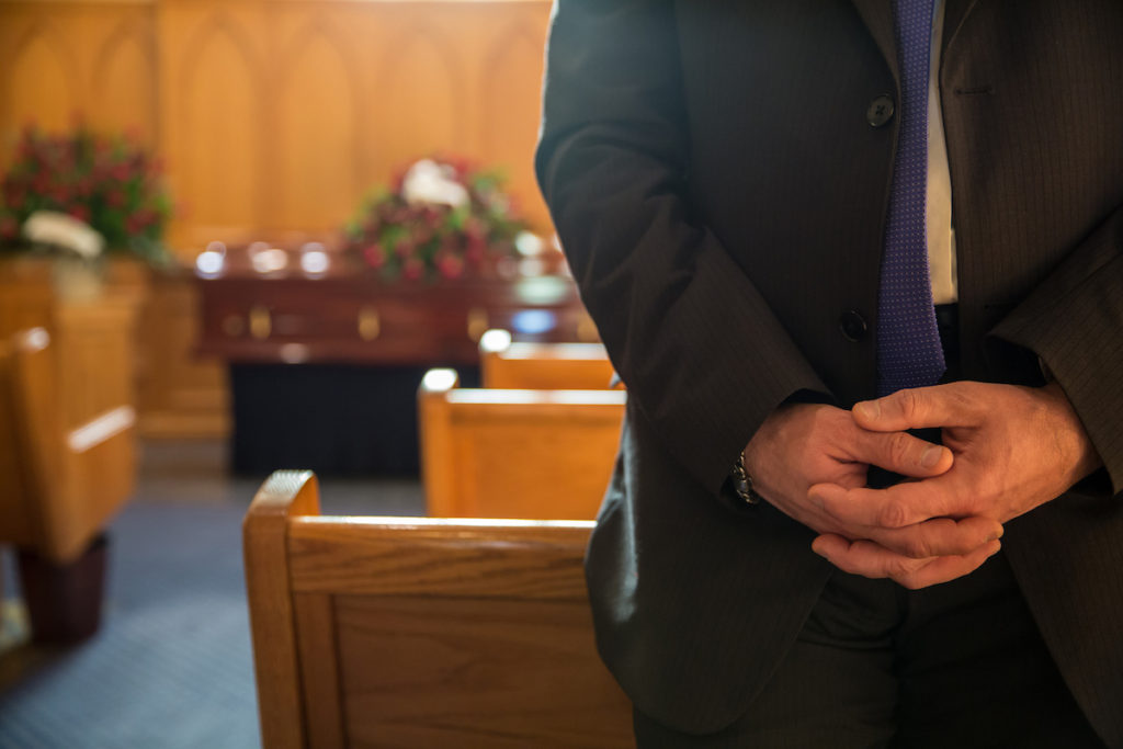Man in suit standing in front of pew at funeral