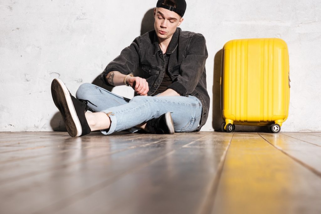 Man looking at watch sitting next to yellow suitcase