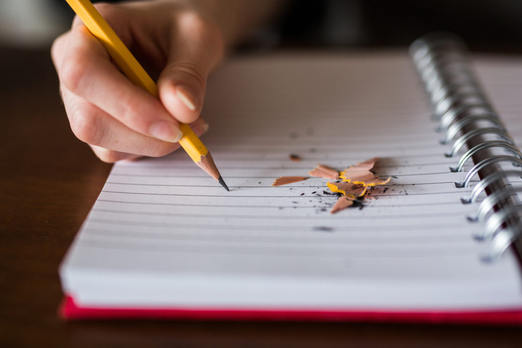 Hand using pencil next to pencil shavings