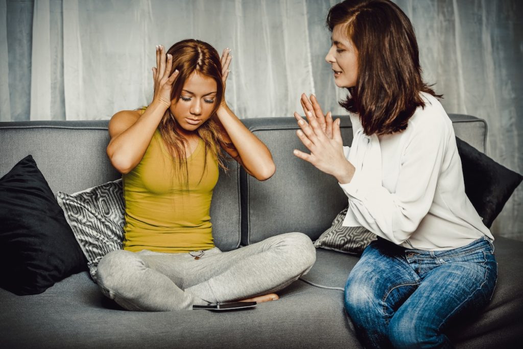 One woman talking to another woman with hands over ears