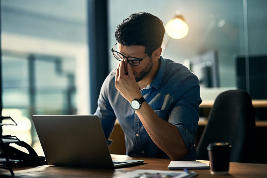 Man looking distressed sitting at table with laptop