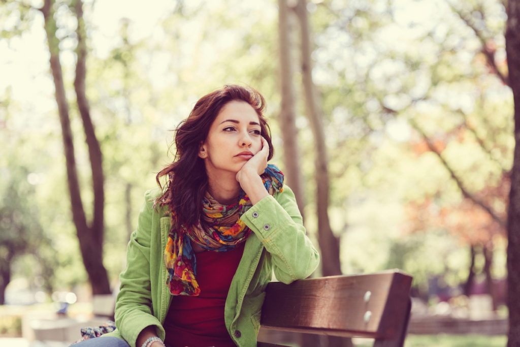 Woman looking sad sitting on bench in park