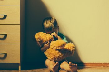 Sad boy sitting down, hugging teddy bear