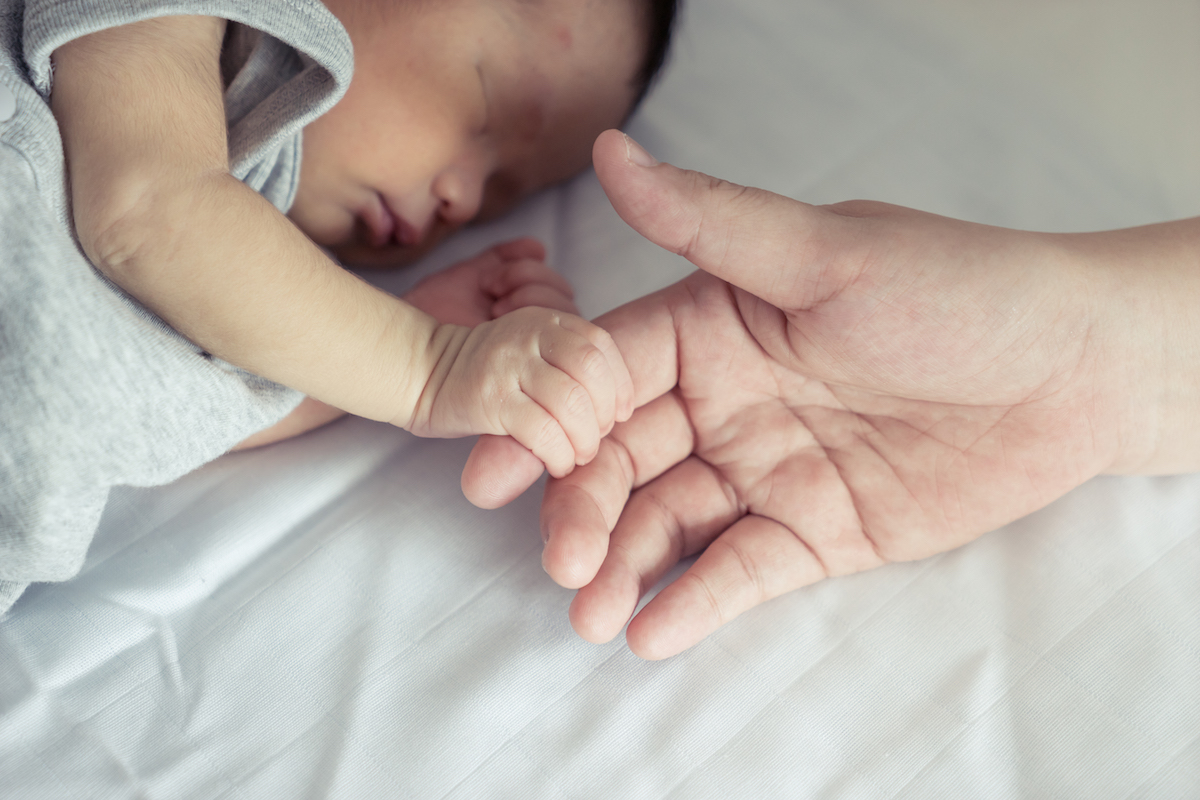 Sleeping baby holding onto mother's finger