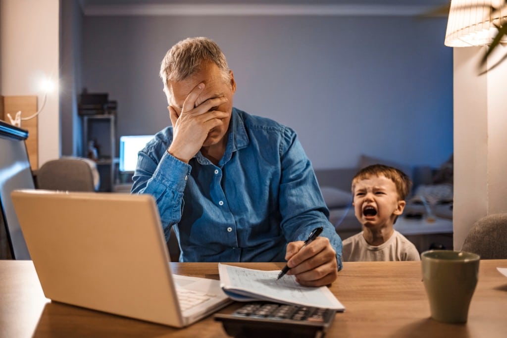 Father at computer with screaming child behind him