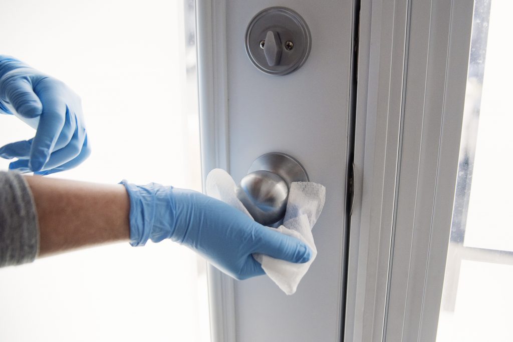Female hands with blue glove wiping doorknob with disinfectant wipe.
