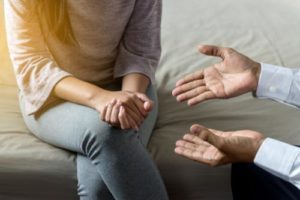 Woman sitting on couch clutching hands, discussing helping a meth addict