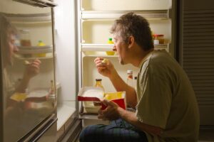 Man eats cake out of fridge, struggling with both addiction and eating disorder