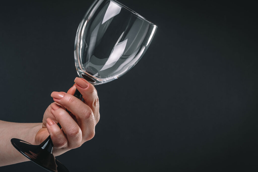 Woman holds empty wine glass as she considers the signs of a drinking problem